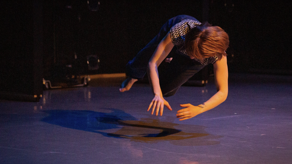 Teresa Fellion during a dance performance hovering above the ground with arms outstretched to form a circle.